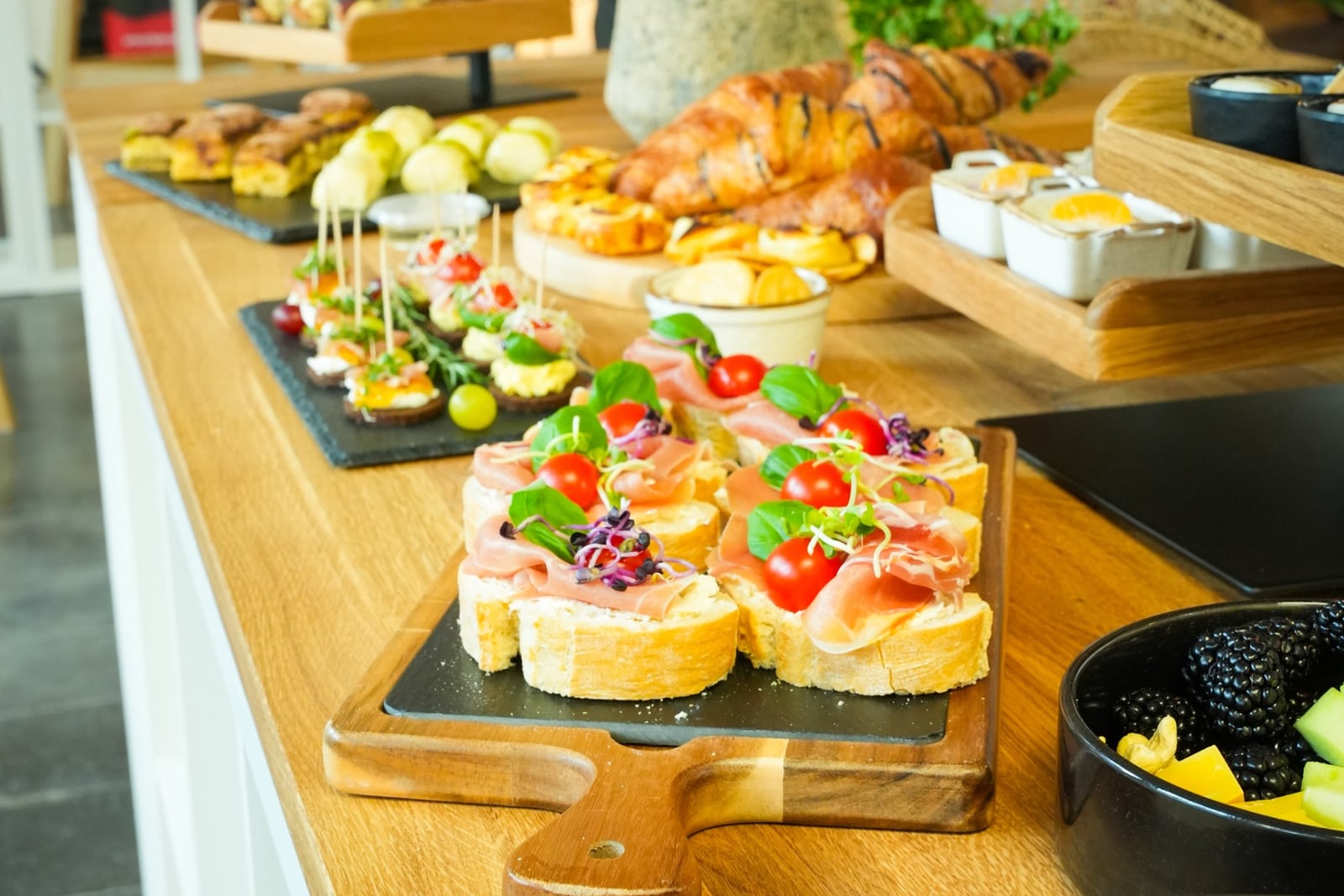Bruschetta mit Schinken, Tomaten und Basilikum, dahinter Fingerfood und Croissants am Buffet auf der Etage