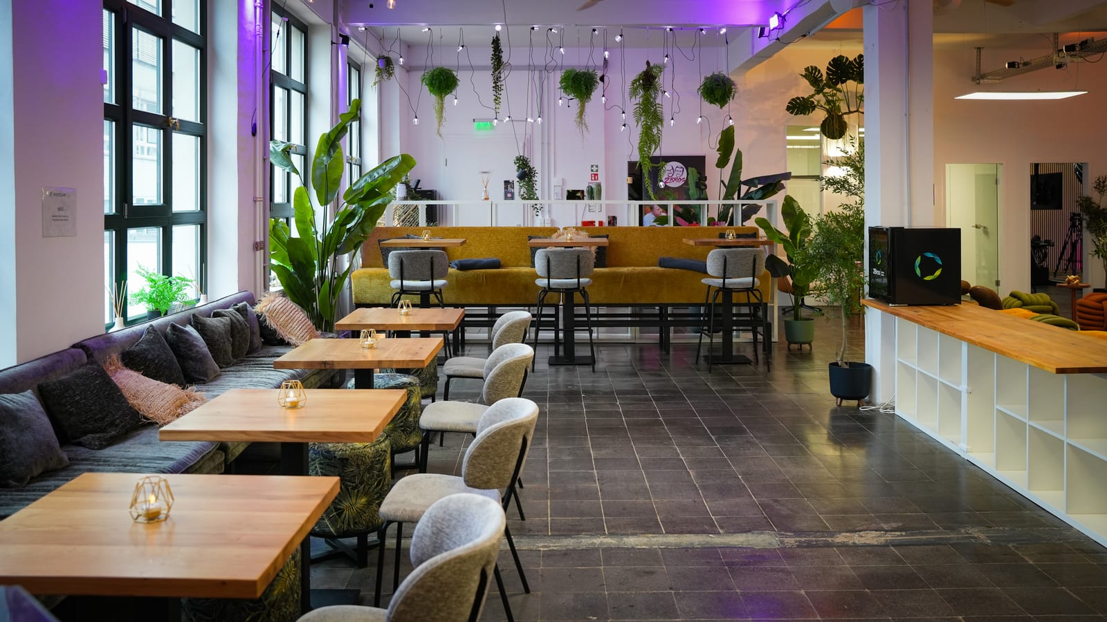 Clubbereich der Etage mit Holztischen, Sofa und großen Fenstern